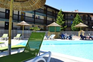 ein Swimmingpool mit Stühlen und Sonnenschirmen neben einem Hotel in der Unterkunft Village Vacances Le Junka in Vieux-Boucau-les-Bains