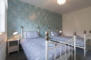 a bedroom with two beds and a blue wall at Kilburn Holiday Cottage in Largs