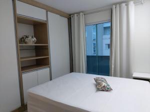 1 dormitorio con cama blanca y ventana en Bem Pertinho do Mar - Cobertura, en Bombinhas