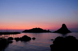 a sunset over a body of water with rocks at Oasis in Acitrezza