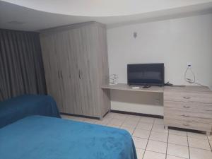 Atlântico Flat Natal في ناتال: غرفة نوم بسرير ومكتب مع تلفزيون