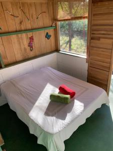 Una cama pequeña con una almohada roja y verde. en Cabañas Casa Soley en Puerto Soley