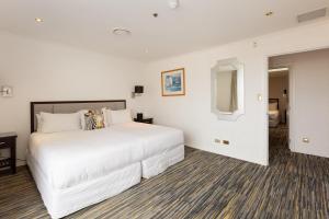 a white bedroom with a large bed and a mirror at Fino Hotel & Suites in Christchurch