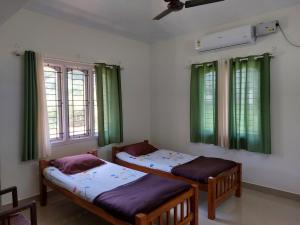 two beds in a room with green curtains and windows at Tharavad Holiday Home in Mangalore