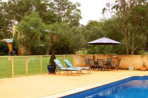 a patio with chairs and an umbrella next to a pool at Chez Vous Split Level Balcony Spa Villa! in Pokolbin