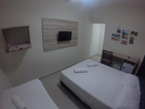 um quarto com uma cama branca e uma televisão em Pousada Praia Cia, Piscina, Centro, Estacionamento, WIFI, Saída até as 16h em Bertioga