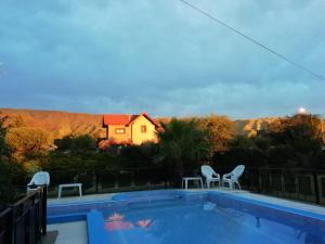 una piscina con 2 sillas y una casa en el fondo en Casa MERLITO - PISCINA DE USO EXCLUSIVO - HERMOSAS VISTAS A LAS SIERRAS -VILLA DE MERLO - SAN LUIS en Merlo