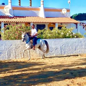 Ein Mann reitet ein weißes Pferd vor einem Haus in der Unterkunft Herdade dos Salgados do Fialho in Faro