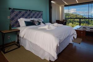 a bedroom with a large white bed with a large window at ÁGUA MARINHA Pousada Caparao in Divisa