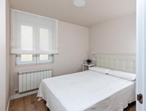 a white bedroom with a white bed and a window at A Tu Lado VUT 09306 in Burgos