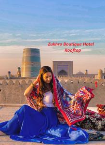 Zukhro Boutique Hotel في خيوة: امرأة جالسة على الأرض أمام مبنى