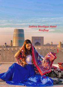 una mujer sentada en el suelo frente a un edificio en Zukhro Boutique Hotel, en Khiva