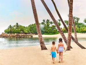 two children walking on the beach under palm trees at Shangri-La Rasa Sentosa, Singapore in Singapore