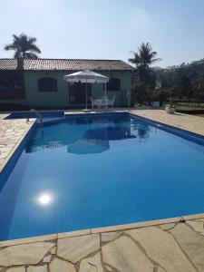 una gran piscina azul con sombrilla en Casa de Campo "Recanto Céu Azul" en Guararema