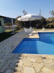 una piscina con sombrilla, mesa y sillas en Casa de Campo "Recanto Céu Azul" en Guararema