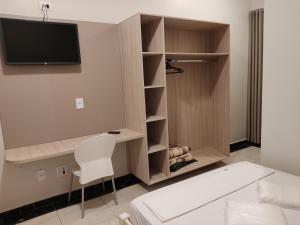 een kamer met een bed, een tv en een witte stoel bij Liv Hotel in Pôrto Ferreira