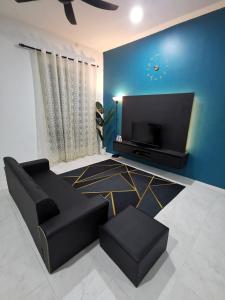 a living room with a black couch and a flat screen tv at LYNN HOMESTAY SERI ISKANDAR in Seri Iskandar