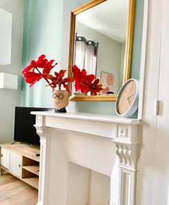 a fireplace with a mirror and a vase with red flowers at Arina & Julien Dieppe in Dieppe