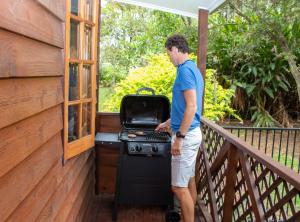 Ein Mann steht neben einem Grill auf einem Balkon in der Unterkunft Sunshine Valley Cottages in Woombye