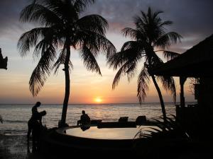 two people sitting in a pool on the beach with a sunset at Paradise Palm Beach Bungalows and Dive Center in Tulamben