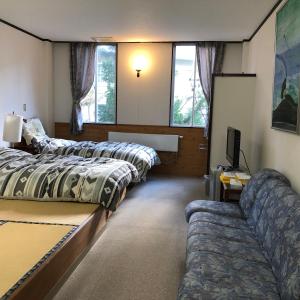 Petit Hotel Yukikkoso في يوزاوا: غرفه فيها ثلاث اسره واريكه