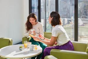 dos mujeres sentadas en una mesa mirando sus celulares en Aparthotel Adagio Access Paris Bastille, en París