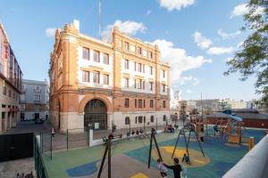 - un grand bâtiment avec une aire de jeux en face dans l'établissement Apartamento Nuestra Andalucia - Cadiz Centro - parking, à Cadix