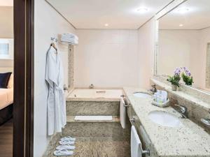a bathroom with a tub, sink, and mirror at Caesar Business Belo Horizonte Belvedere in Belo Horizonte