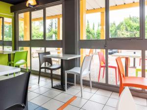 un restaurant avec des chaises, des tables et des fenêtres colorées dans l'établissement ibis budget Nimes Caissargues, à Caissargues
