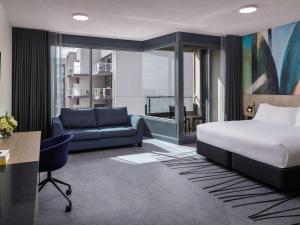 a bedroom with a bed and a couch and a desk at Novotel Geelong in Geelong