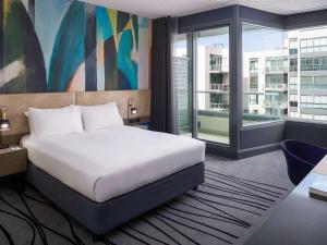 a bedroom with a white bed and a large window at Novotel Geelong in Geelong