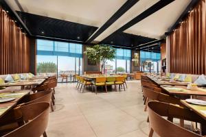 um restaurante com mesas e cadeiras de madeira e janelas grandes em Wyndham Garden Ajman Corniche em Ajman