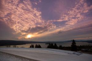 a sunset over a snowy field with the sun in the sky at Rangeley Lake Resort a Ramada by Wyndham in Rangeley