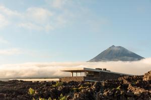 a building on a hill with a mountain in the background at Azores Wine Company in Cais do Mourato