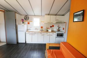 eine Küche mit weißen Geräten und einer orangefarbenen Wand in der Unterkunft Camping La Tentation in Renty