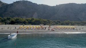 um barco na água ao lado de uma praia com guarda-sóis em Villaggio Camping Odissea em Marina di Camerota