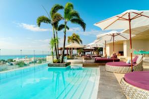 a beach area with a pool, chairs, and umbrellas at Thompson Playa del Carmen - Adults Only - a concept by Hyatt in Playa del Carmen