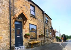 um edifício de tijolos com uma porta azul e um banco em The Wynd Cottage em Amble