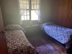 twee bedden in een kleine kamer met een raam bij Cabana Austríaca no Vale Encantado in Campos do Jordão