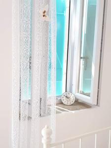 a window with a white curtain and a clock on a window sill at STATHIS GUESTHOUSE in Lefkada Town