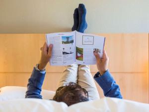 a person laying on a bed reading a book at ibis Lausanne Crissier in Lausanne