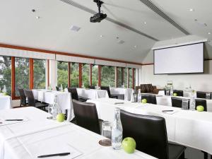 Fairmont Resort & Spa Blue Mountains MGallery by Sofitel في ليورا: قاعة اجتماعات بطاولات بيضاء وكراسي وشاشة