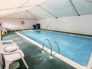 a large swimming pool with white chairs and a swimming poolomy at Swallows Cottage in Walton East