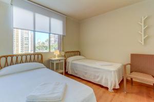 a bedroom with two beds and a chair and a window at Ranchos Apartment in Benidorm