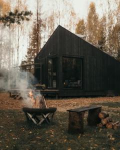 a black cabin with a fire in front of it at Briežu Stacija Off Grid Cabin in Līgatne