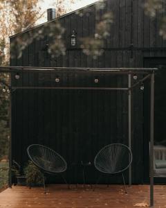 duas cadeiras sentadas em frente a uma cerca preta em Briežu Stacija Off Grid Cabin em Ligatne