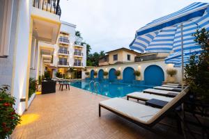 Alvorada Resort-3 Star Resort In Baga في آربورا: مسبح الفندق مع كراسي الصالة ومظلة