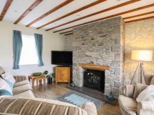 a living room with a stone fireplace and a tv at Tyn Towyn - Ty Coch in Trearddur