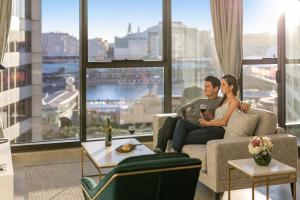 een man en vrouw zittend op een bank in een woonkamer bij Meriton Suites Sussex Street, Sydney in Sydney