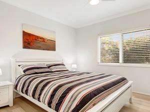 a white bedroom with a bed and a window at Windspray in Culburra Beach